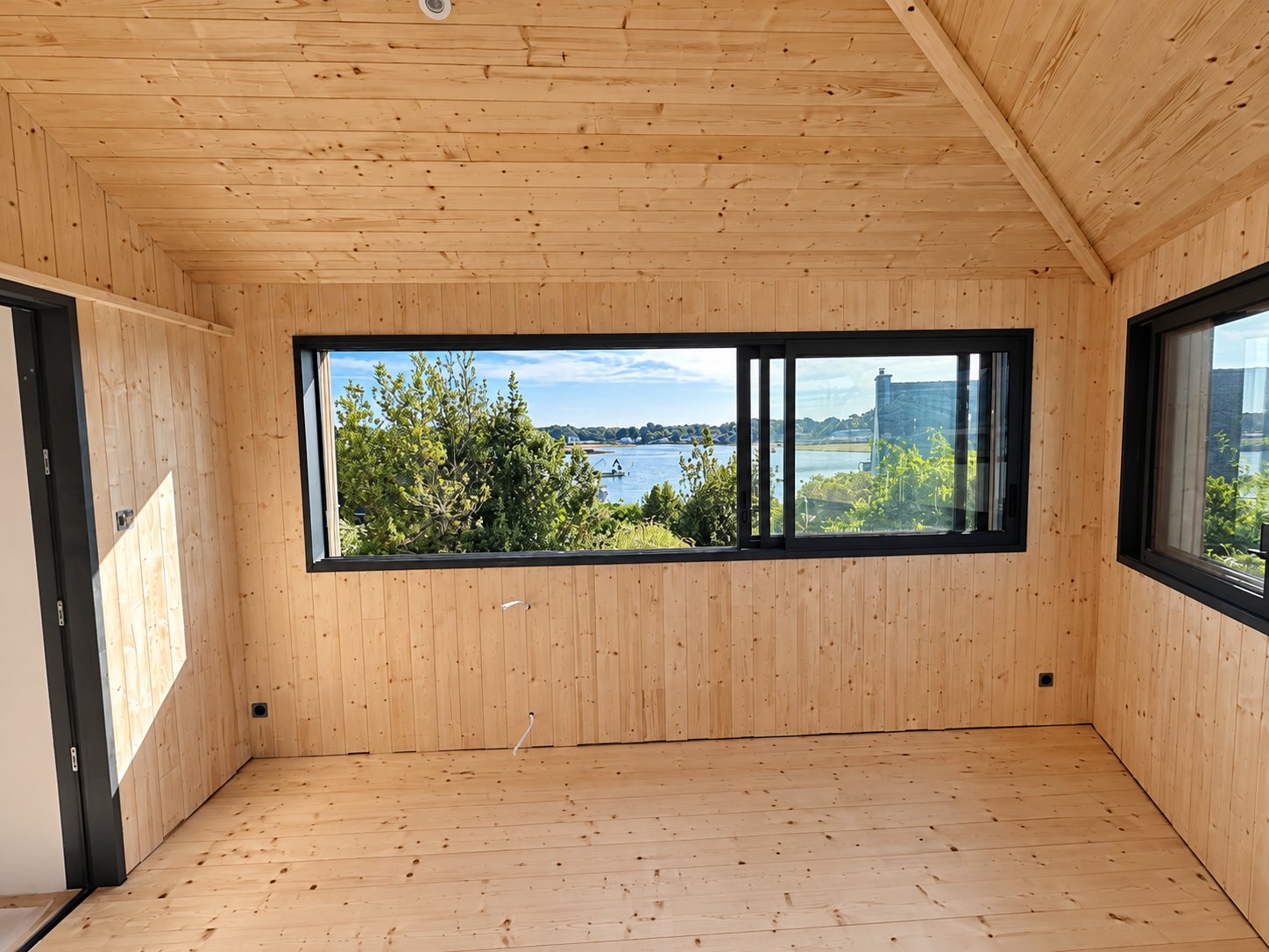 Baie vitrée coulissante en aluminium noir dans une extension en bois, avec vue sur la ria.