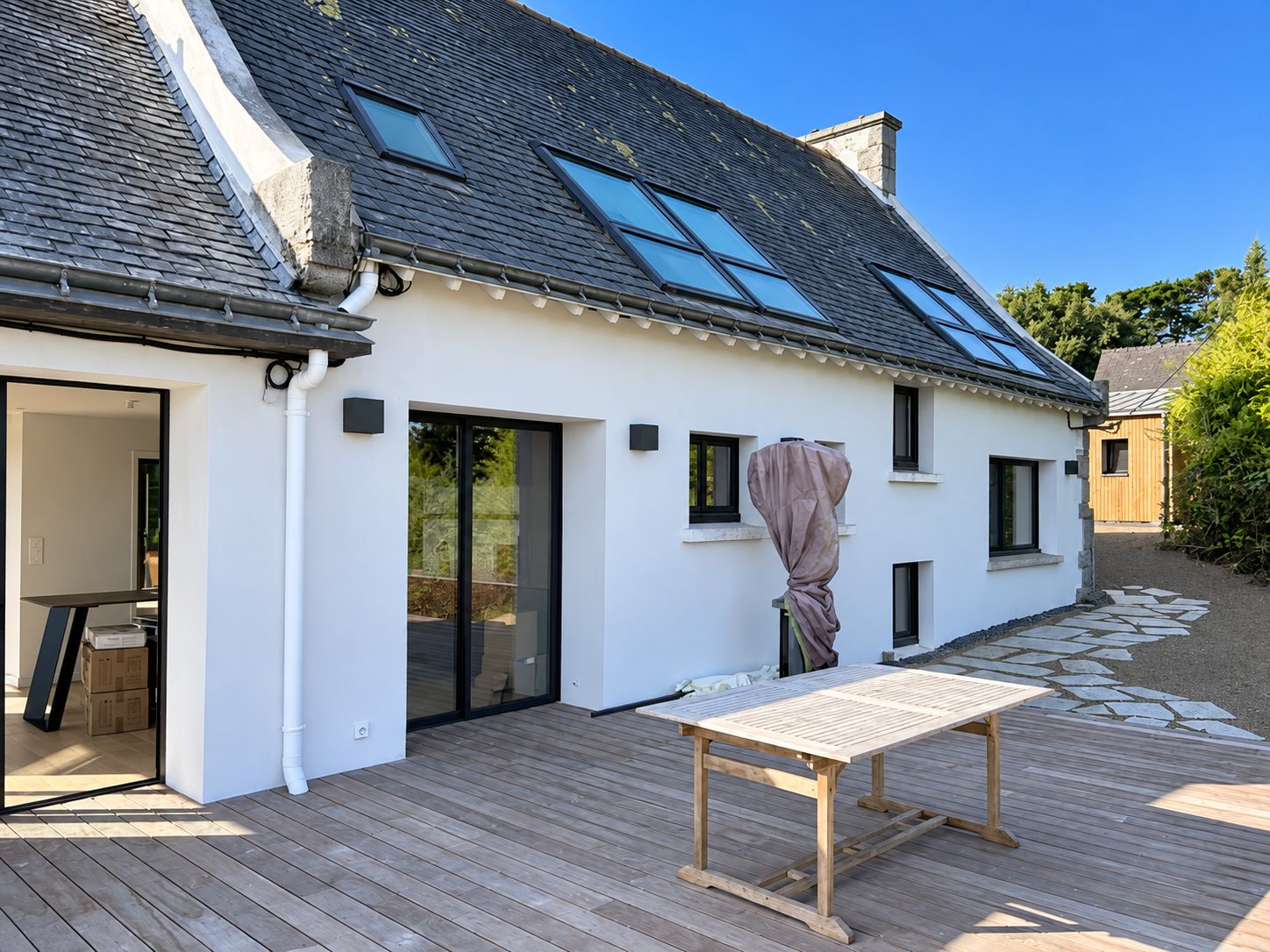 La même maison rénovée : façade blanche, toit d’ardoise, terrasse en bois.