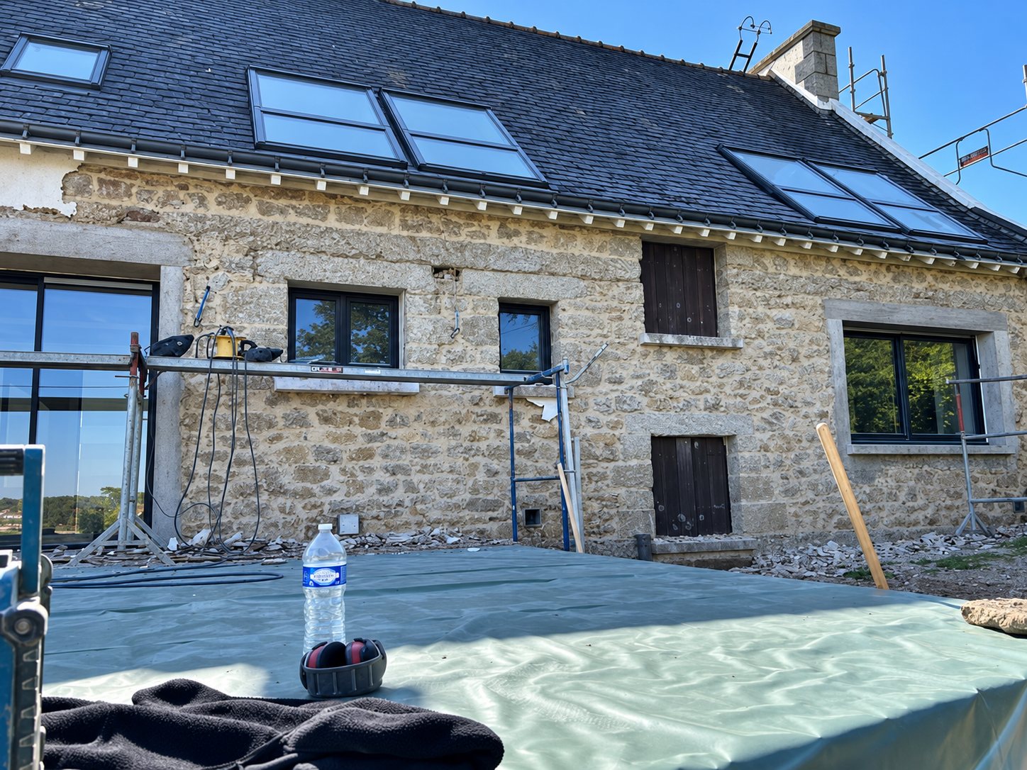 Longère en pierre en chantier, avec échafaudage et fenêtres de toit neuves.